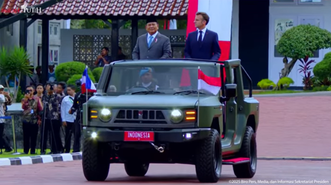 Presiden Prabowo mengenakan setelan jas berwarna abu-abu serta peci hitam berdiri di sisi kanan. Sementara Presiden Macron mengenakan setelah jas biru tua berdiri di sisi kiri. [YouTube Sekretariat Presiden]