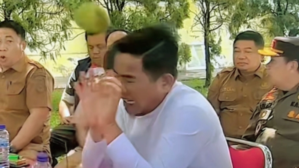 Ekspresi Bupati Pelalawan Zukri saat nyaris ketiban mangga kala memimpin rapat di ruang terbuka. [TikTok]